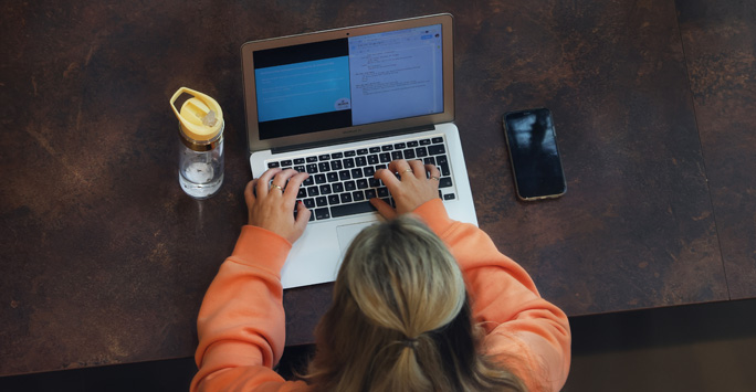 A student sat a table typing on a laptop