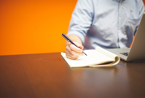 person with laptop, writing on piece of paper