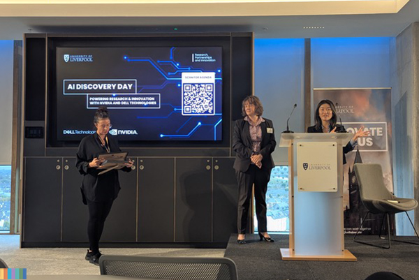Three people on a stage, one standing behind a lectern.