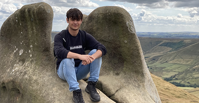 A person posing for a photo, sitting on a big rock.