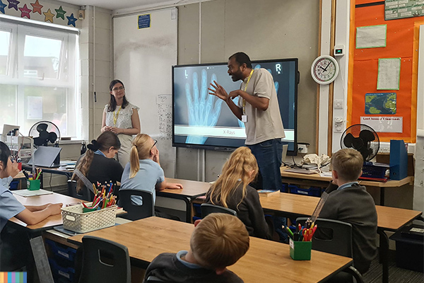 Two students talking to school children in a class room.