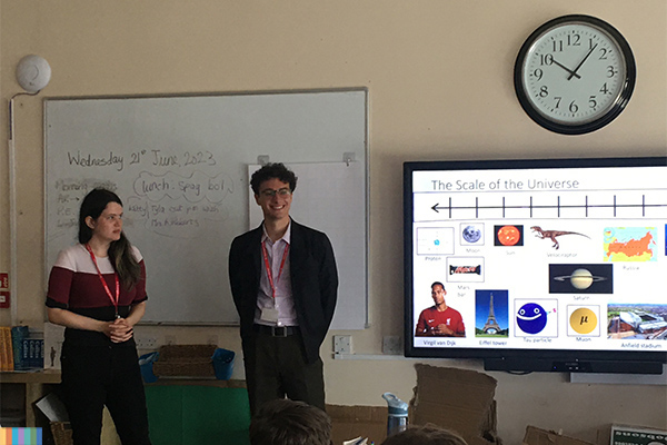 Two students talking to school children in a class room.