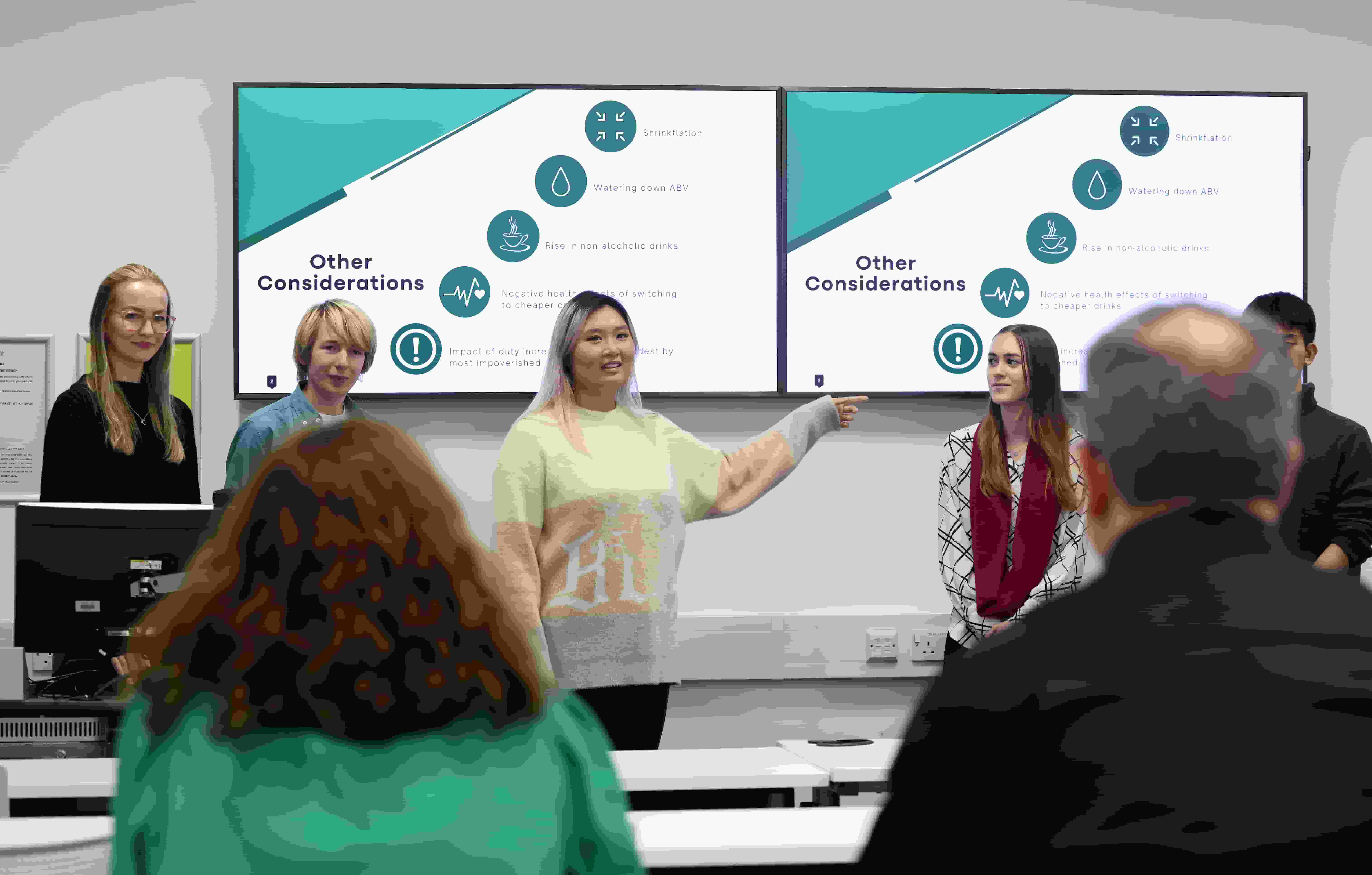 A classroom scene with a group of people attentively watching a presentation displayed on a screen.