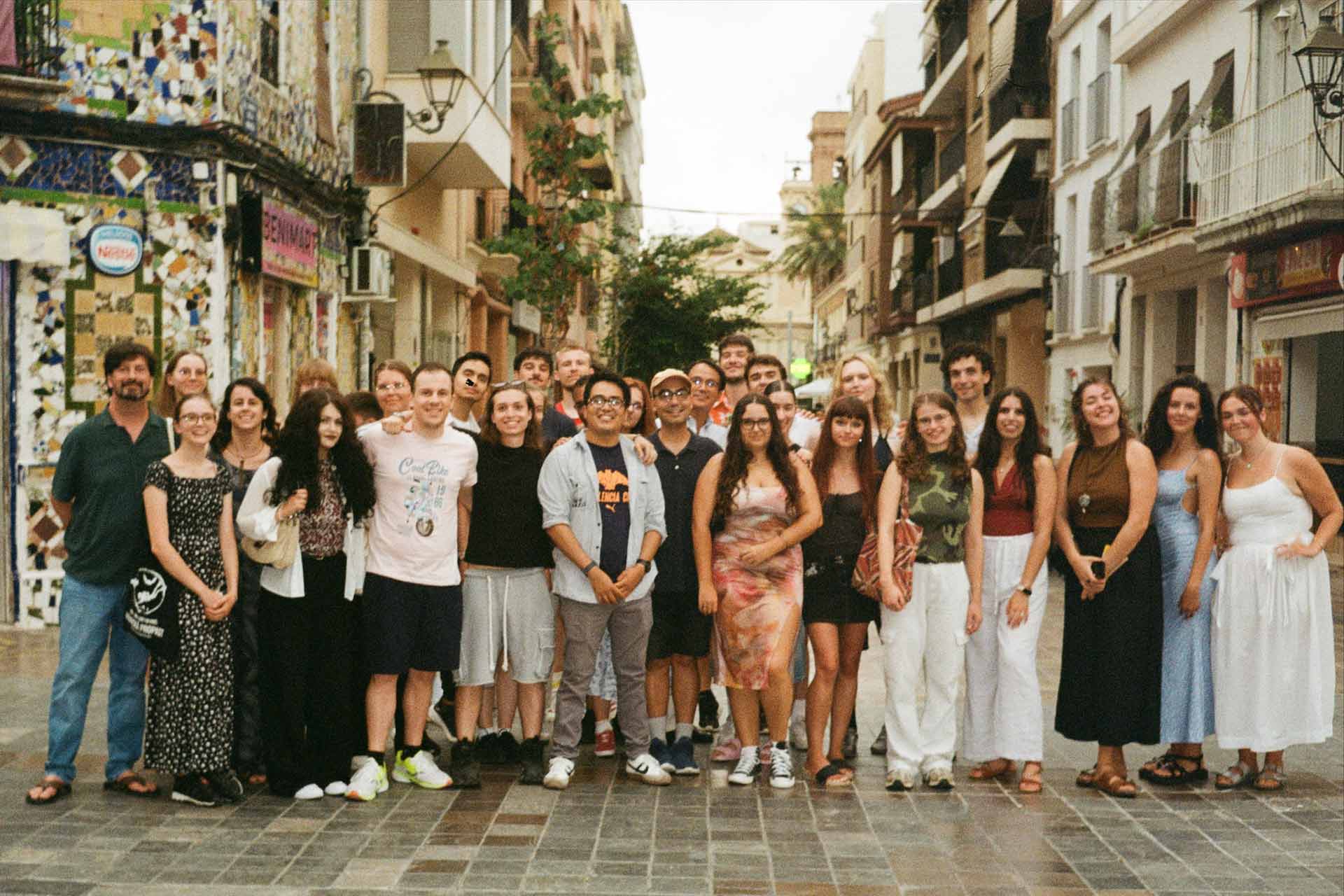 A group of young people standing outside on a European street wearing summer clothes.