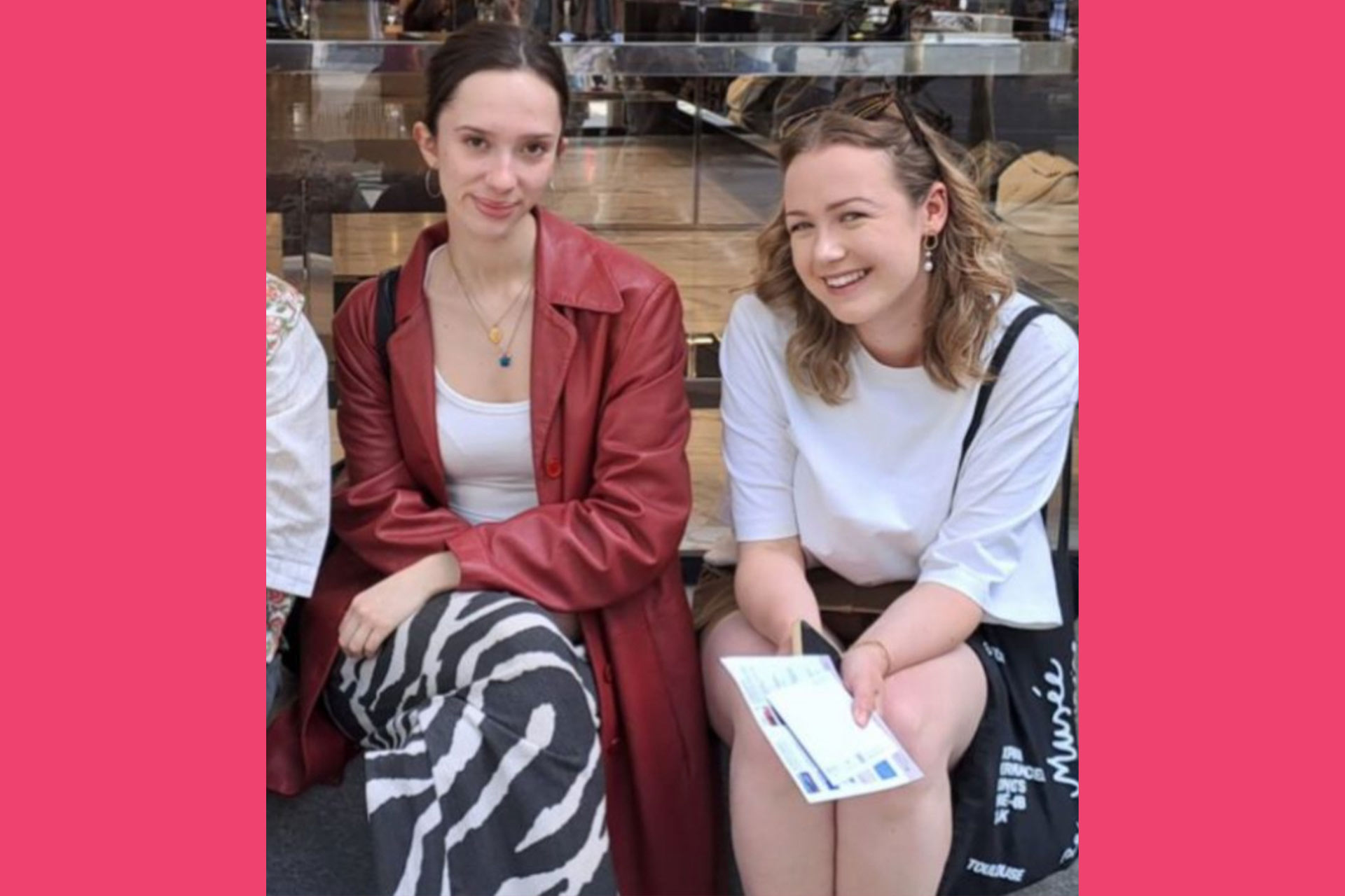 Two brown haired young women sitting together and smiling.