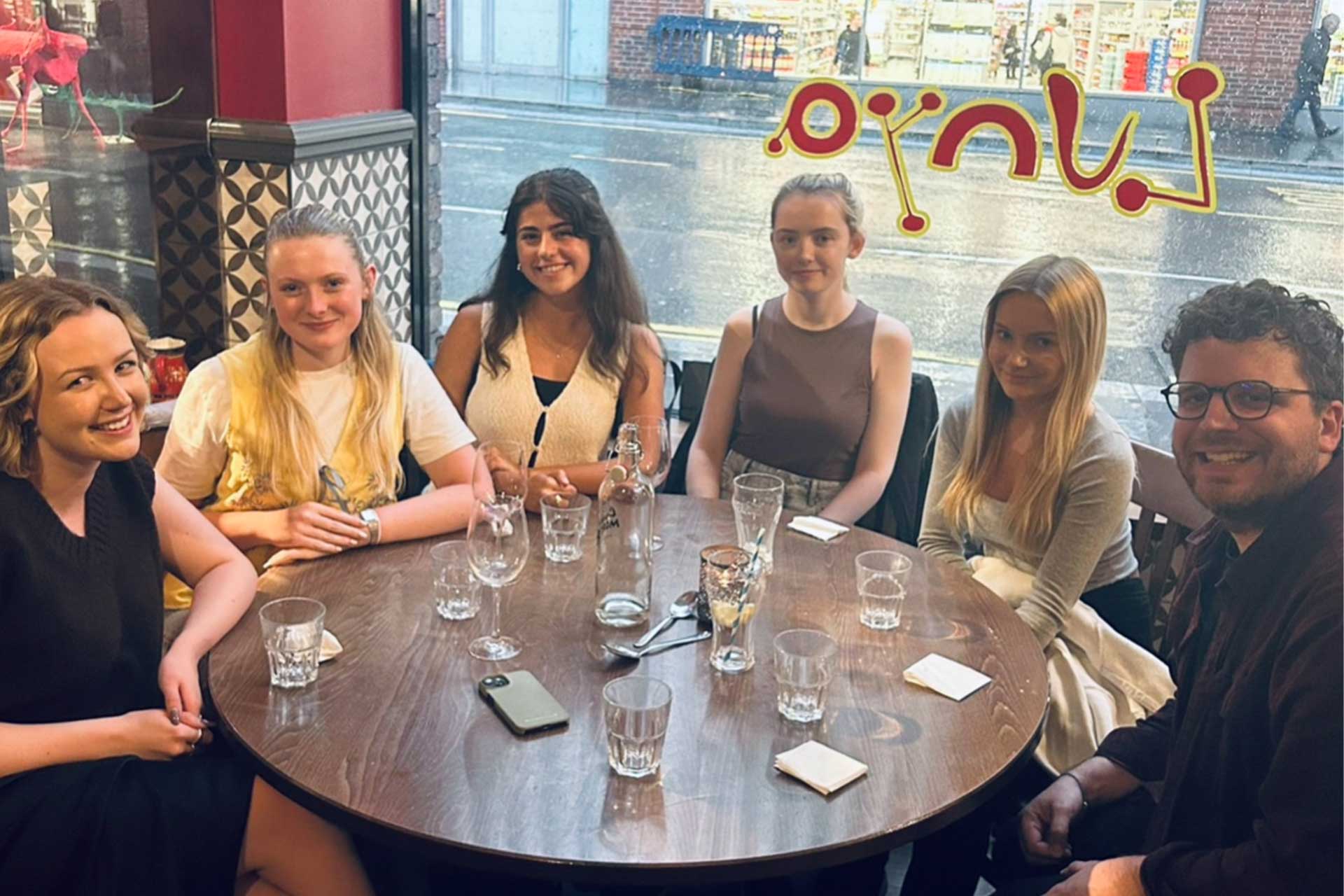 A group of people sat together in a restaurant around a circular table smiling.