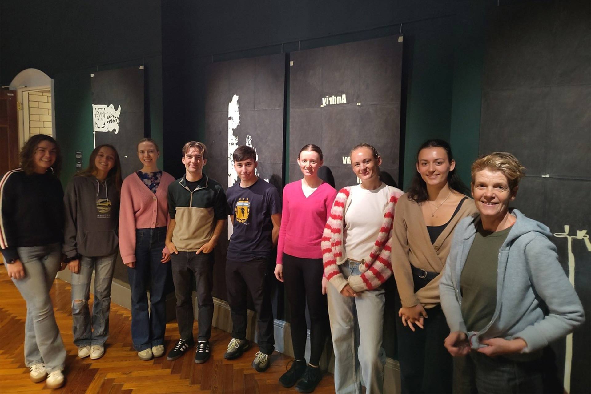 A group of people standing inside an art exhibition room in a line smiling.