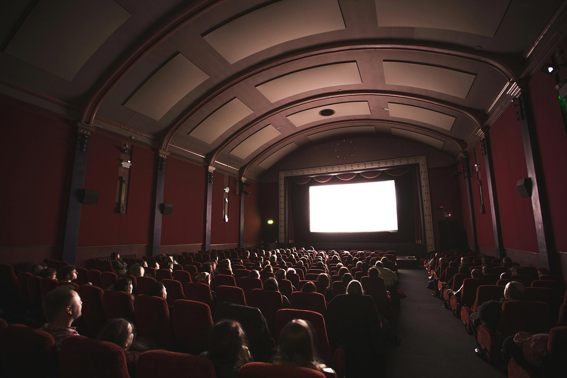 An old cinema, with a large screen at the front and seats with people sitting facing the screen.