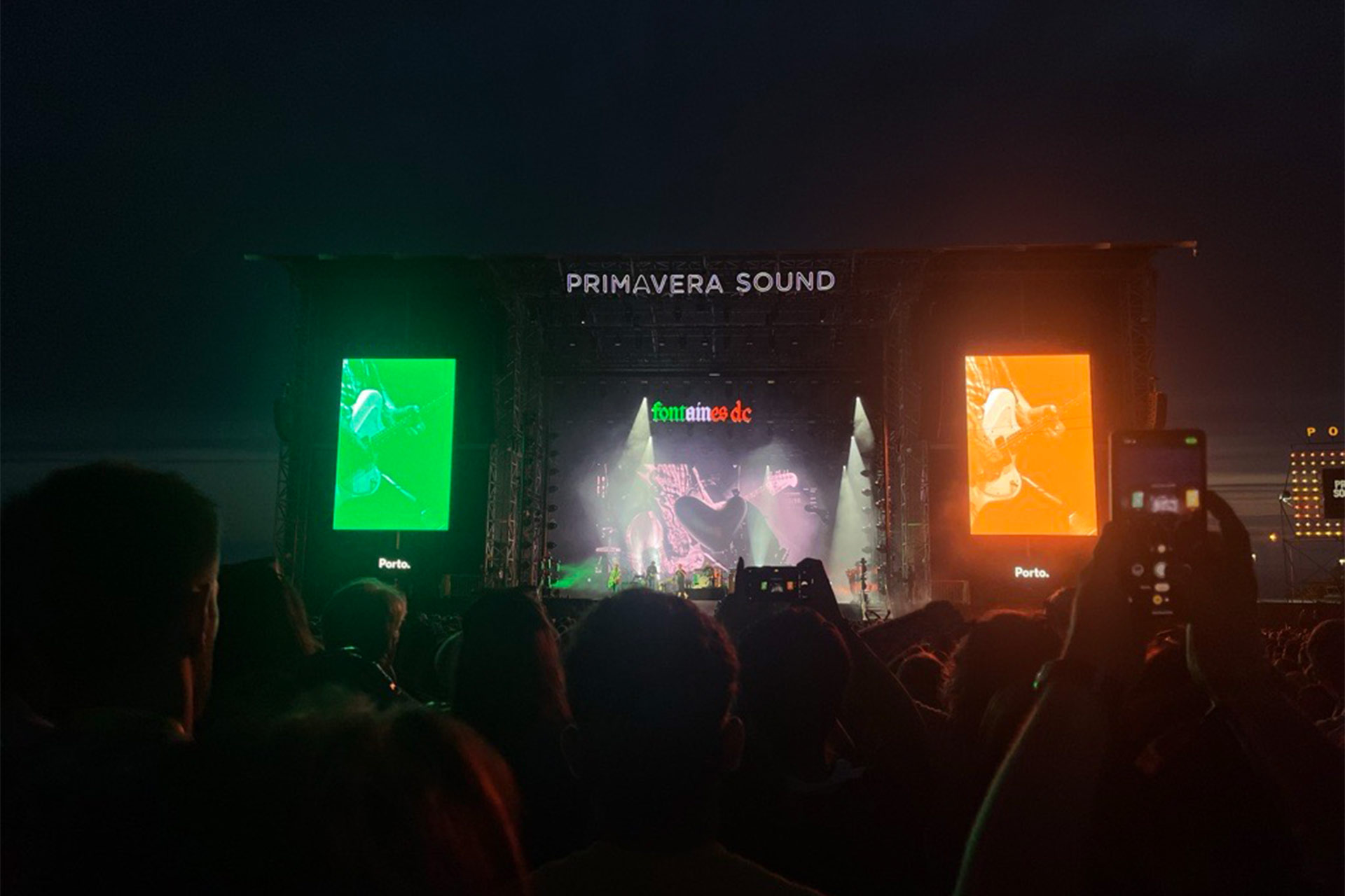A stage at nighttime at a music festival. A main sign over the stage reads 'Primavera Sound', beneath that a band is on stage and a sign reads 'Fontaines DC'.