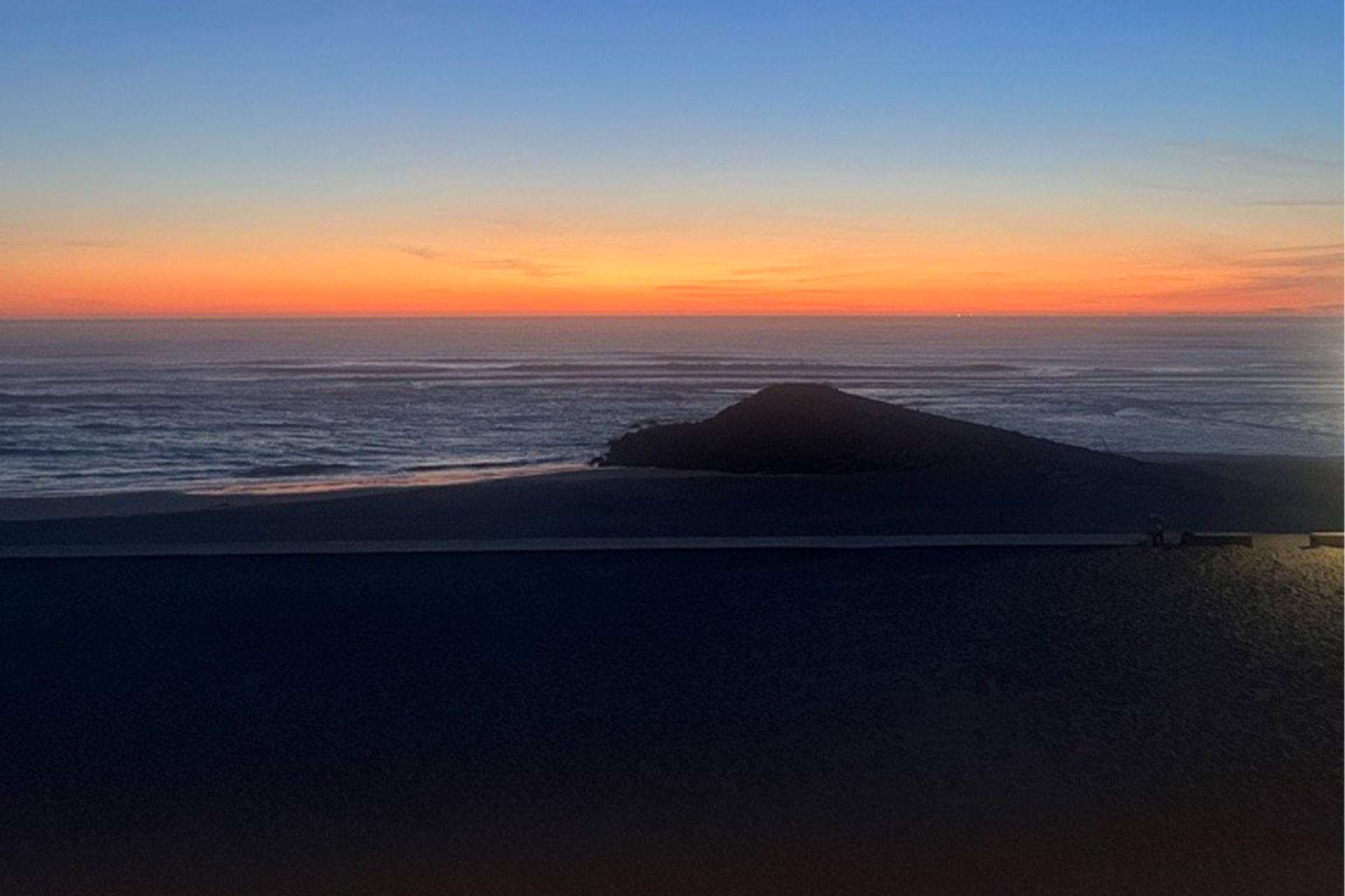 A sunset over a body of water, the land in front is dark.