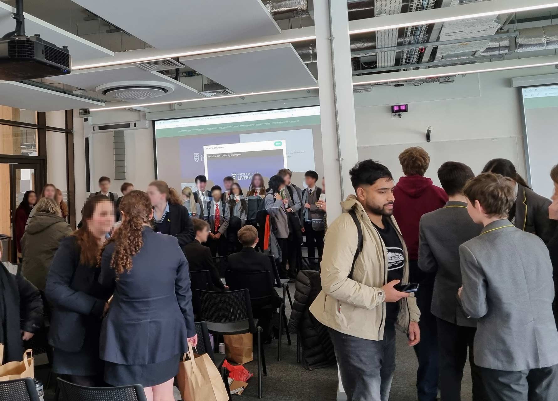 A room of schoolchildren talking to each other and a group of children gathered at the front of a projector screen