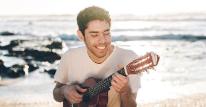 Brazilian musician Luca Argel playing guitar on a beach