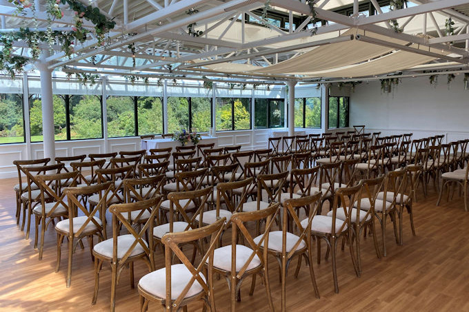 The Hulme Conservatory set for a wedding, with rows of chairs facing a table in front of windows overlooking the gardens.