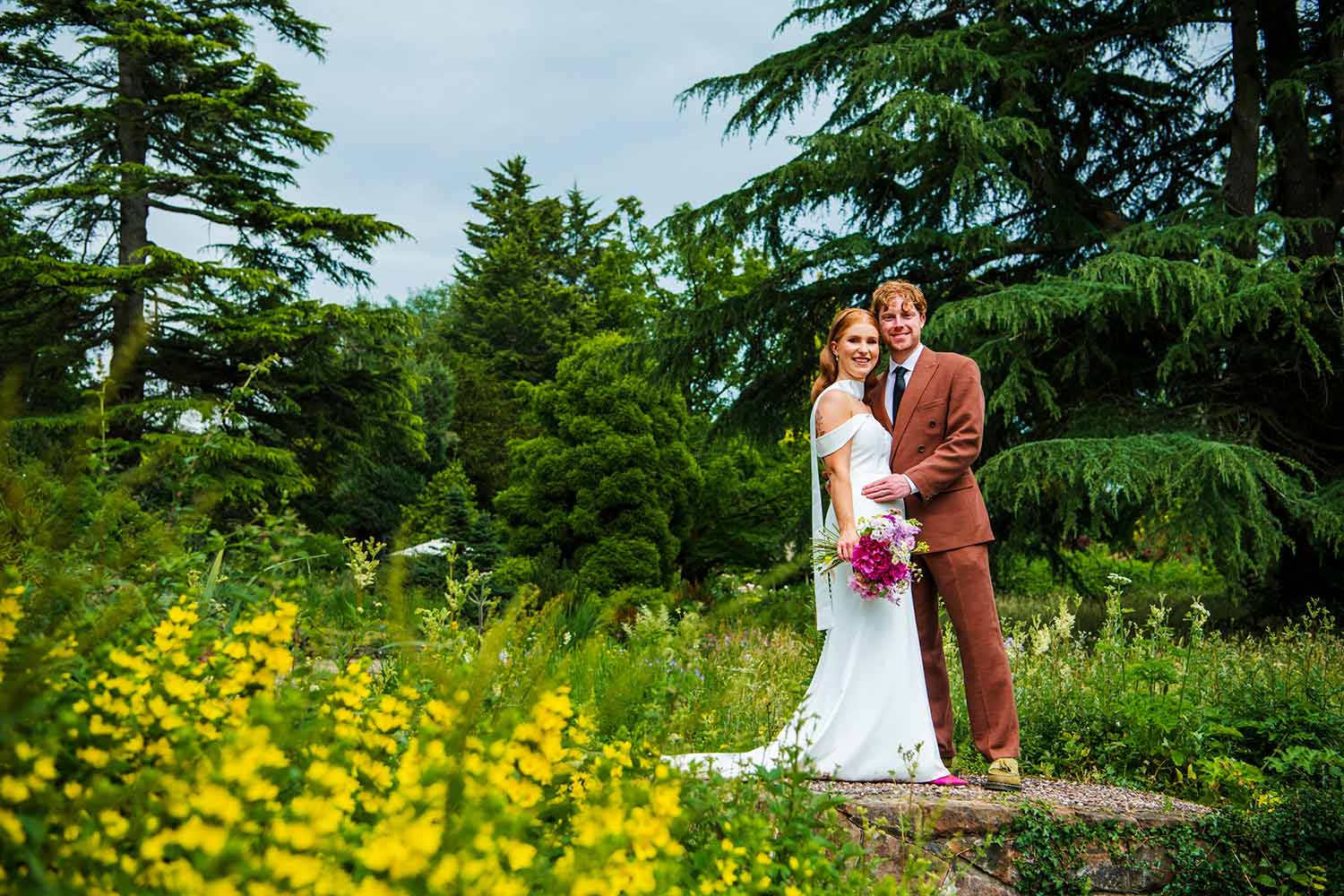 A couple pose for a photo, surrounded by the stunning greenery of Ness, as they wander the gardens after their wedding ceremony.