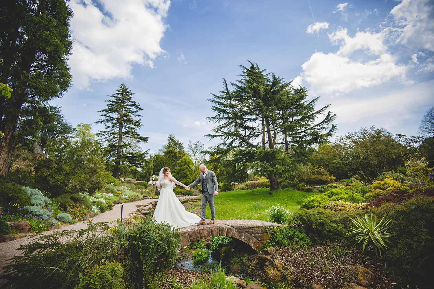 A bride leads a groom over a small bridge as they walk through spectacular scenery at Ness.