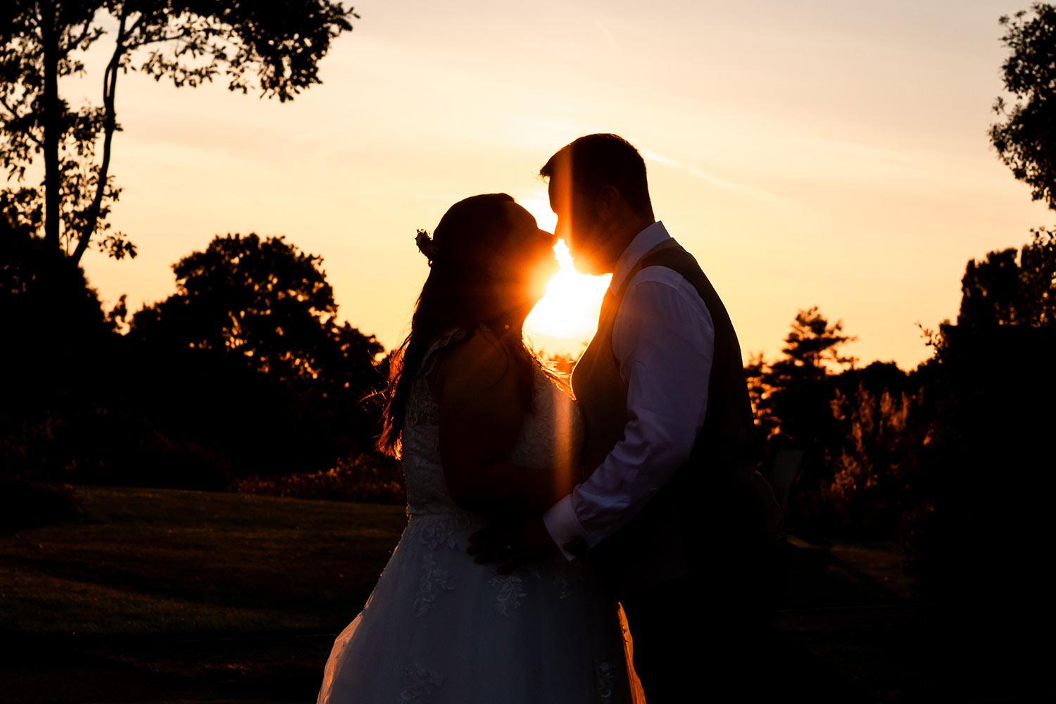 Silhouettes of a couple kissing at dusk at the end of their wedding day.