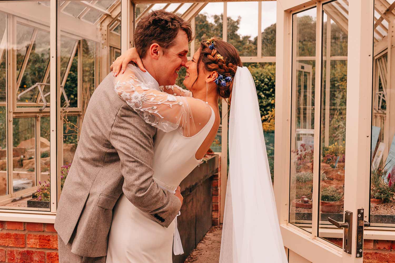 A couple kiss in front of a greenhouse after their wedding ceremony.