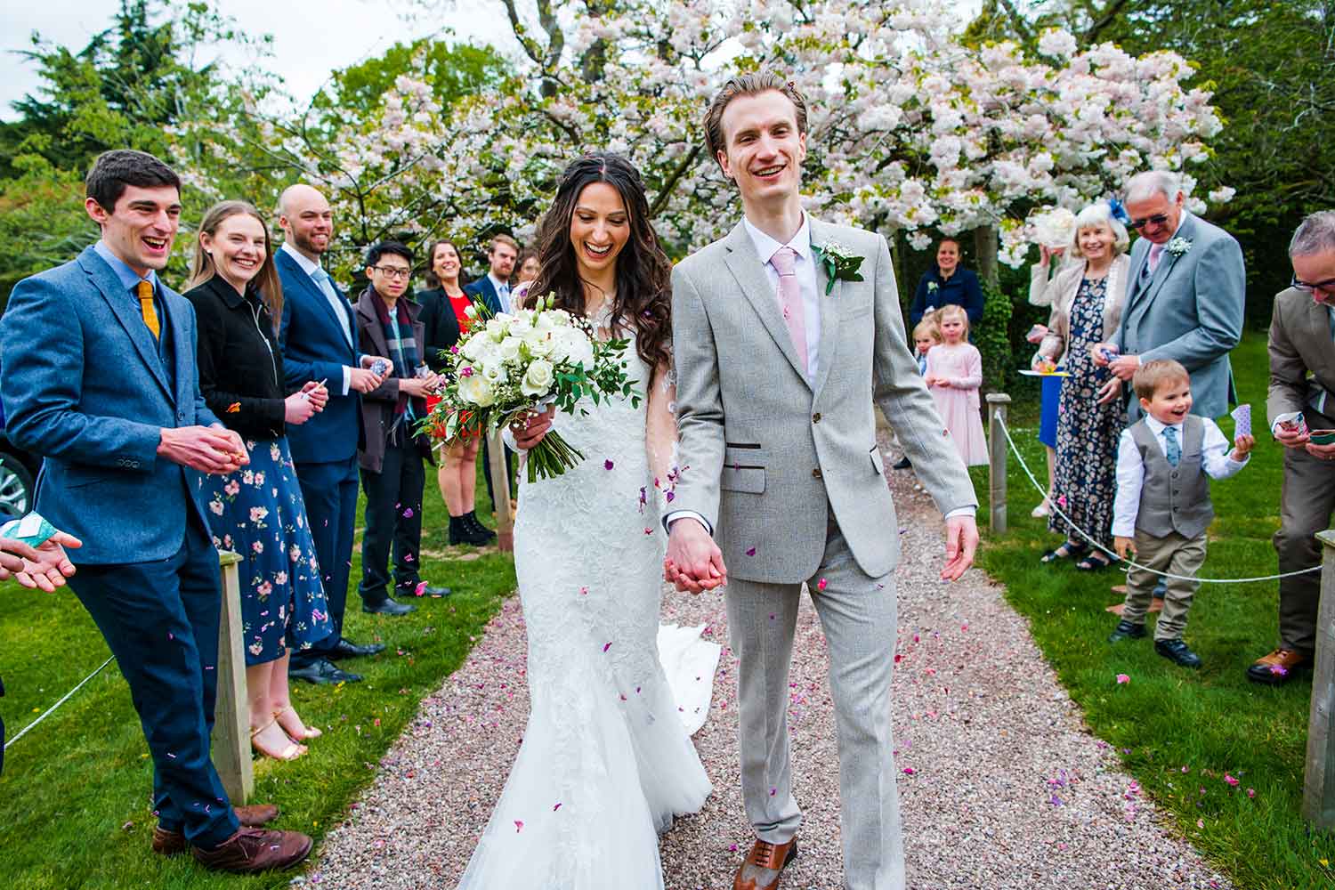 A couple walk along a pathway, cheered by wedding guests on either side.