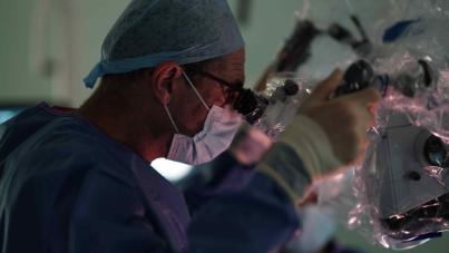 Image of a surgeon in theatre using equipment. Credit: The Walton Centre – Trauma Room One production