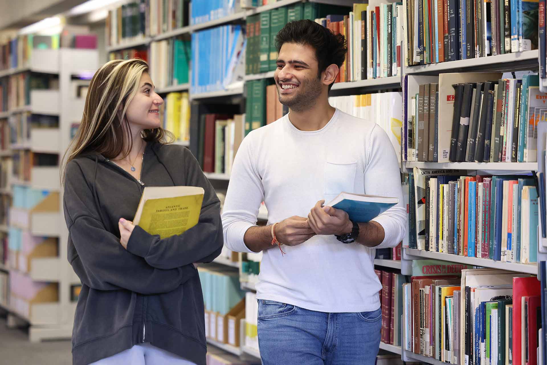 Two students walking through the library carrying books.