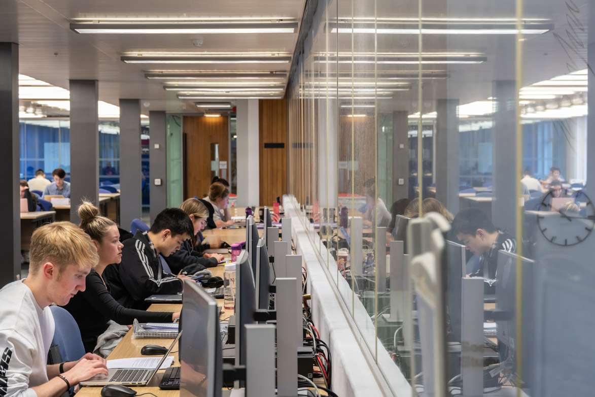 Students working at a row of computers within a library on the University of Liverpool campus