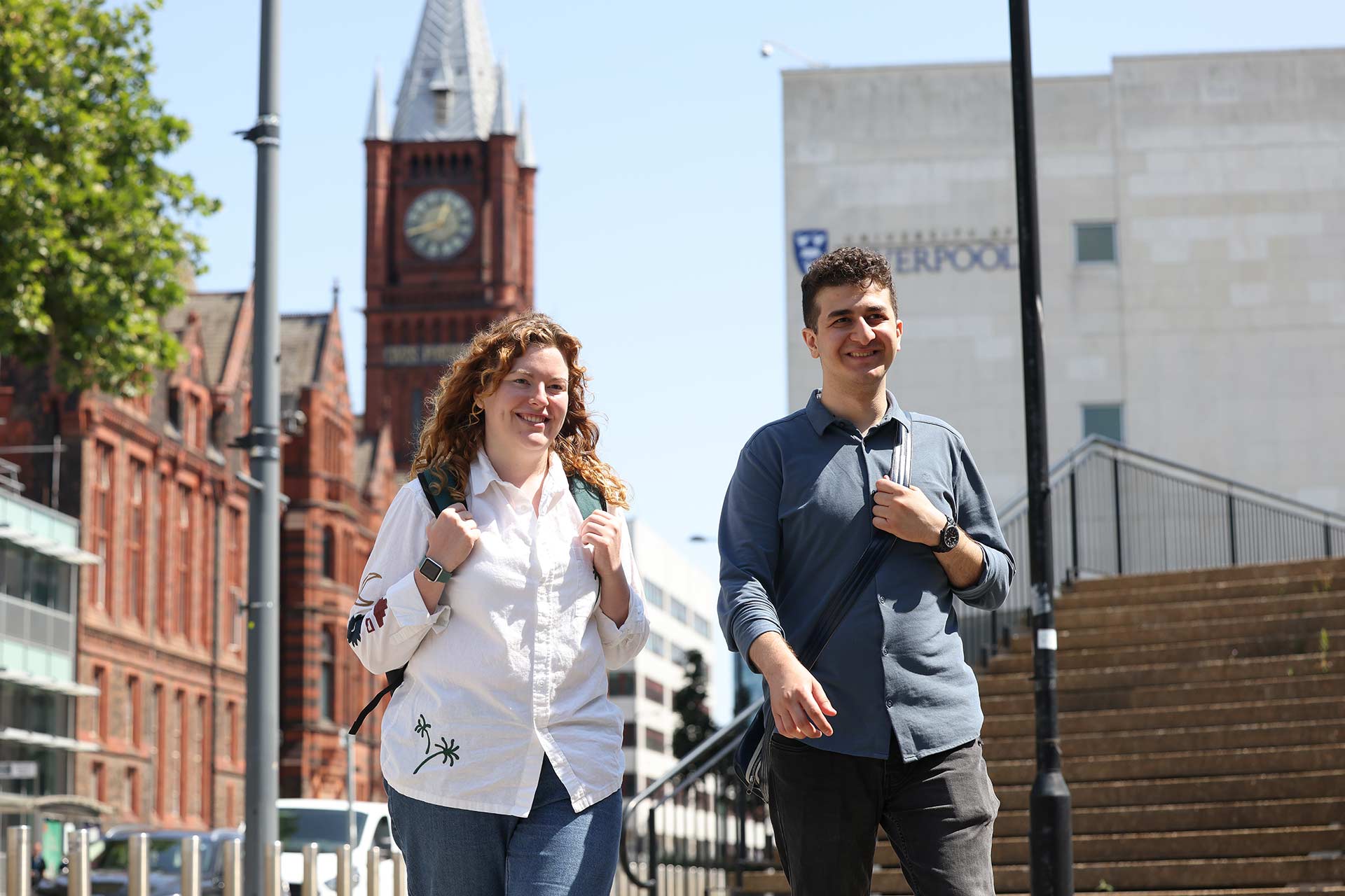 Two postgraduate students walking together on the University of Liverpool campus, the Victoria Gallery and Museum is visible in the background