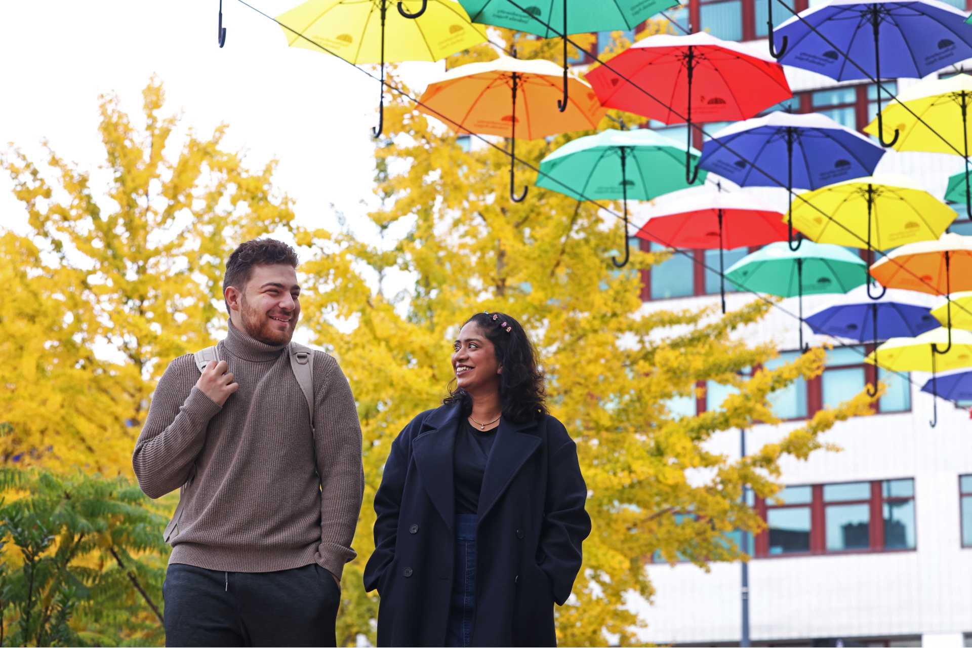 Two students are walking across University Square with the umbrella display in the background.