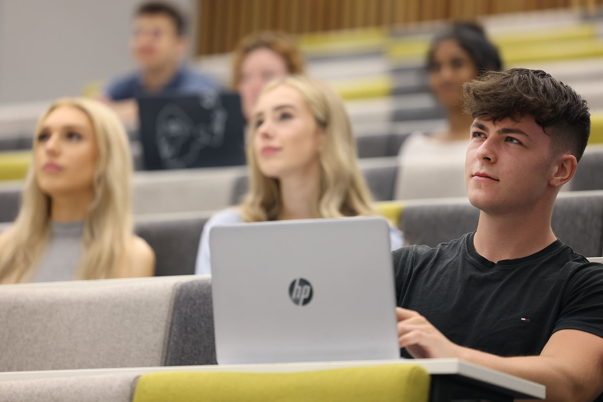 Students sitting in a lecture theatre, student in main focus is using a laptop
