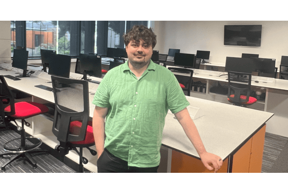 Charlie Devlin stands in front of a computer desk, focused on the screen, in an office setting