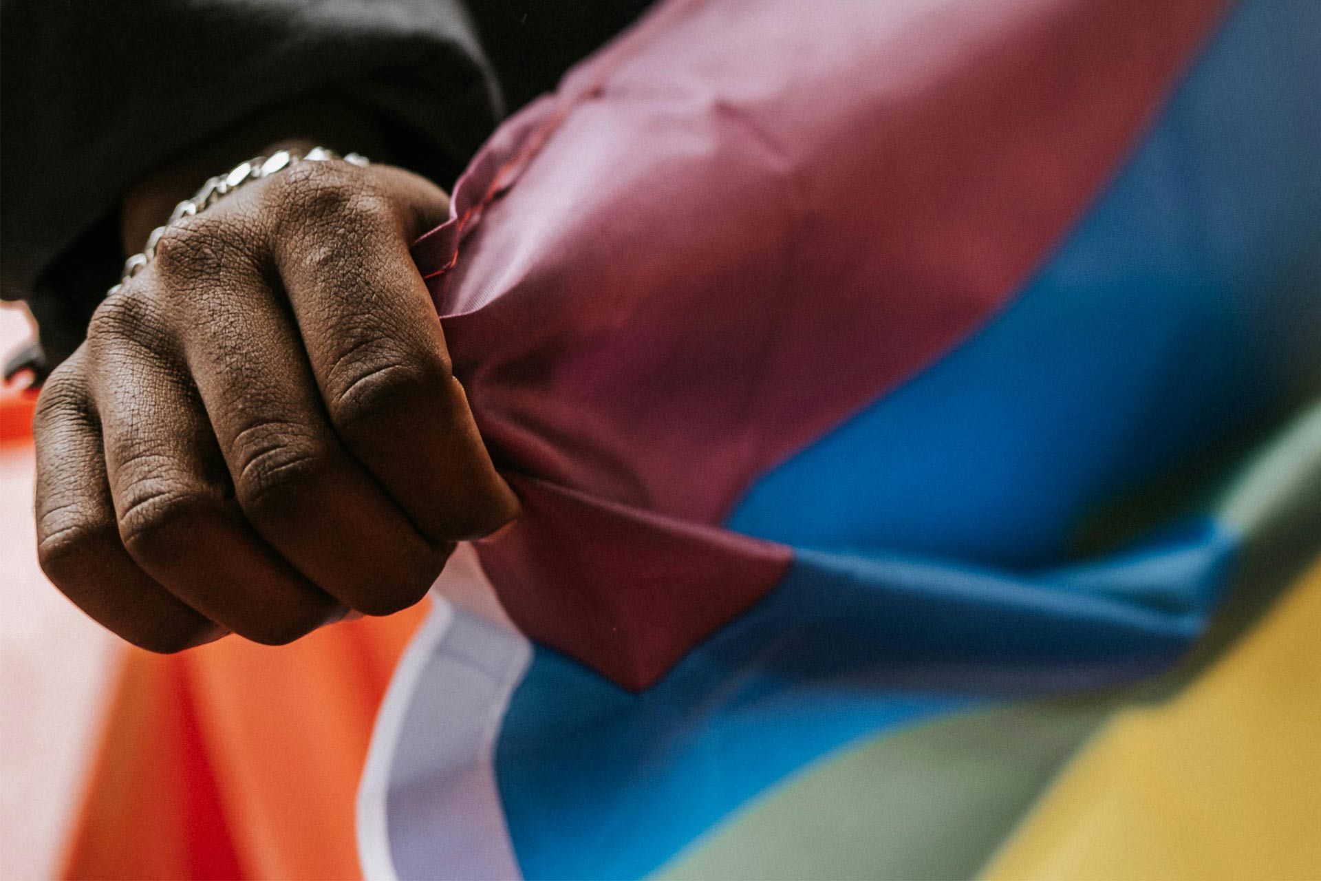 A black hand holding a rainbow flag