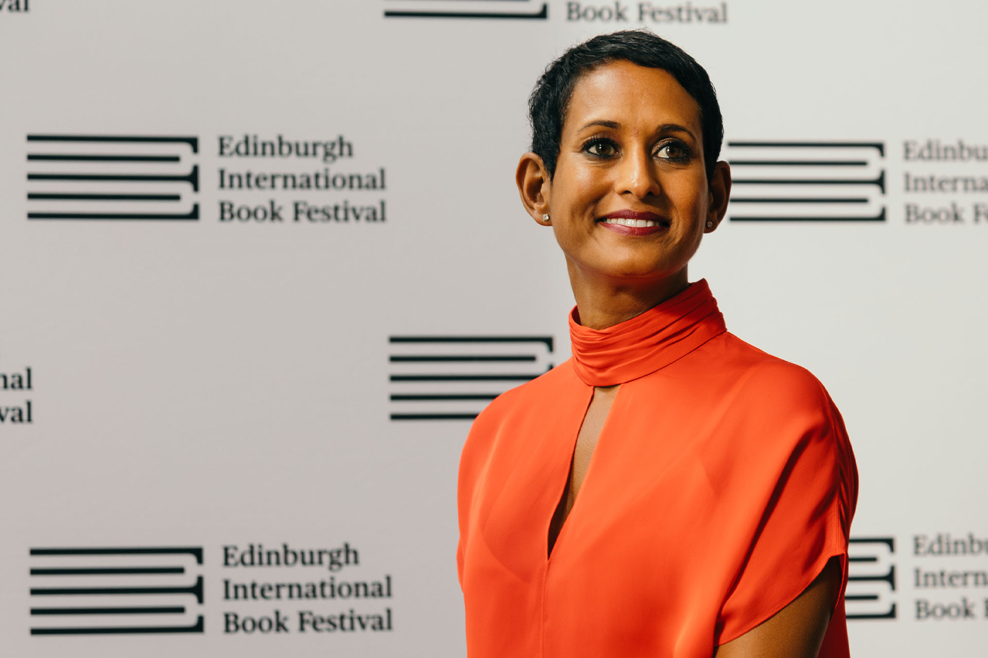A woman with short hair and a bright orange dress smiling.