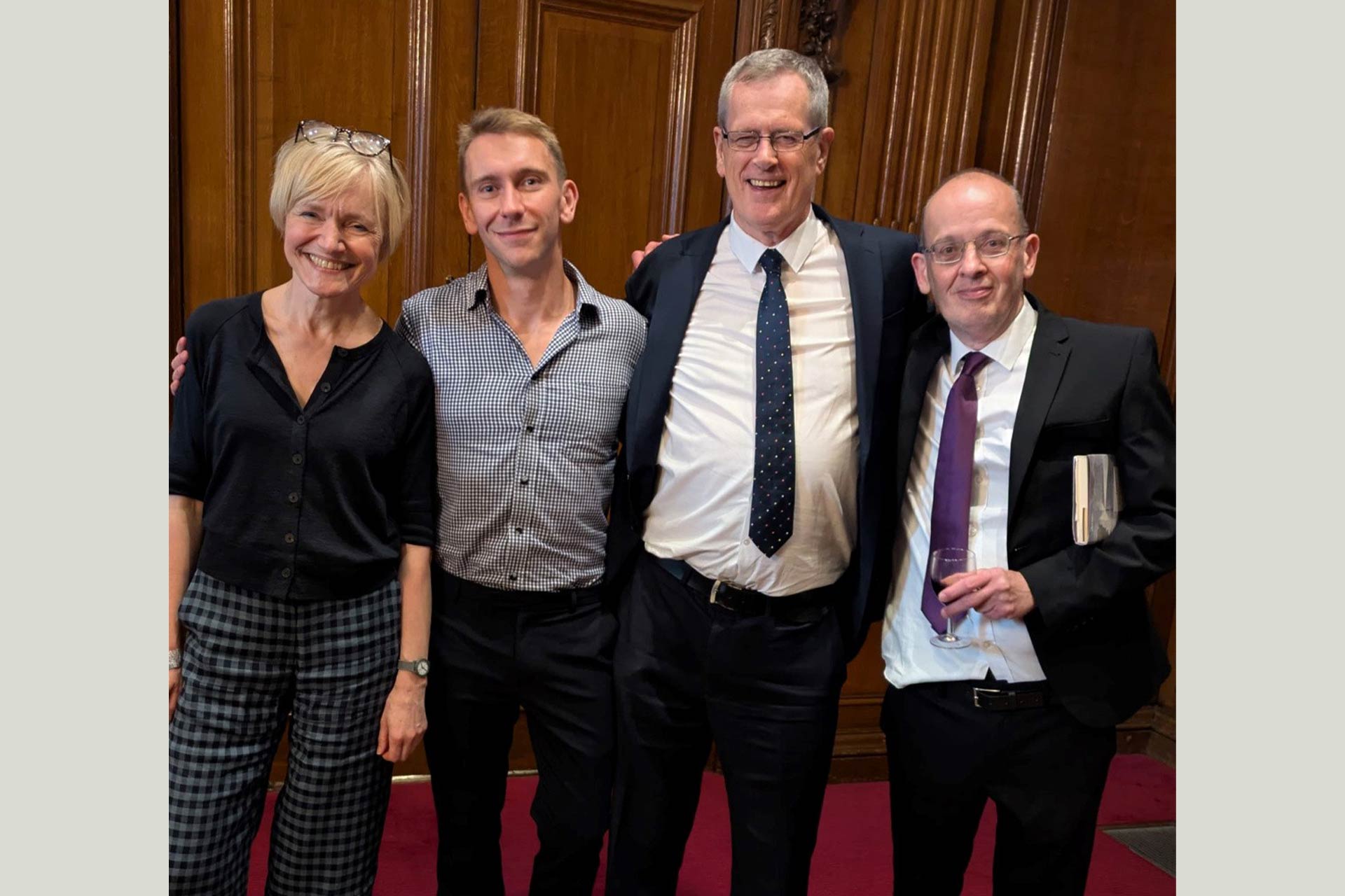 Four people dressed smartly in an wooden panelled room standing together and smiling for a picture
