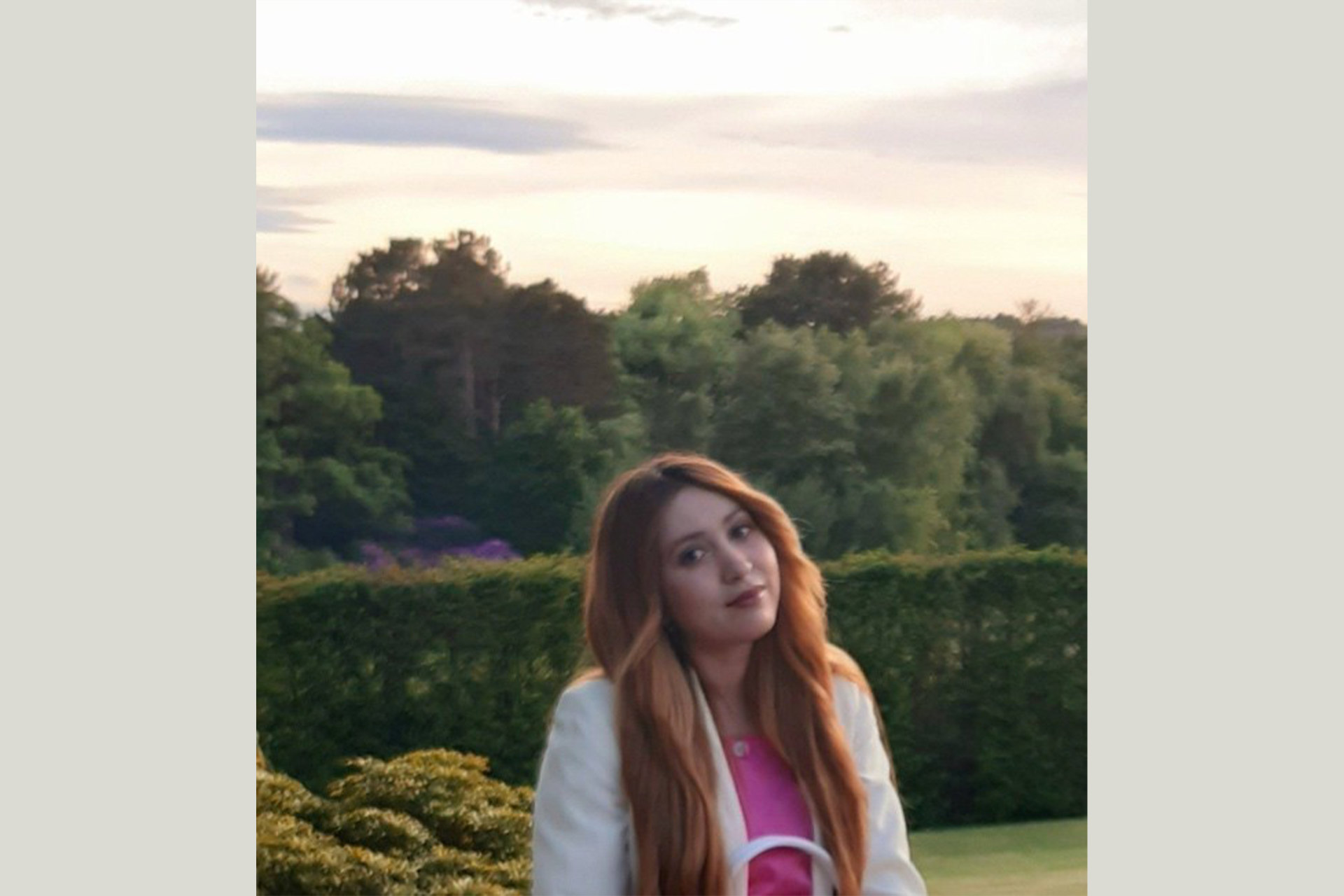 A woman sitting in a green rural area as the sun sets, smiling at the camera.