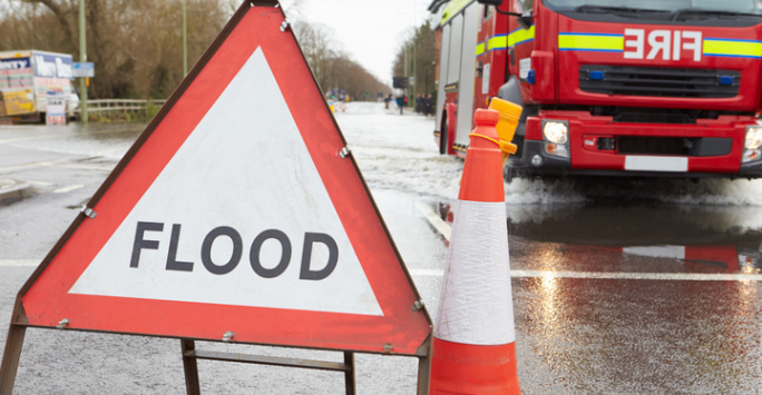 Flood sign in front of a flooded road, fire engine in the background