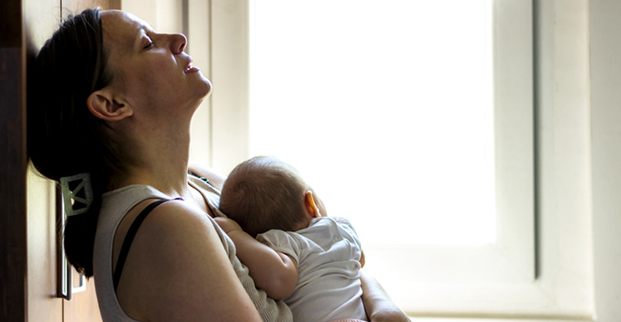 Picture of a new mother resting her head back whilst holding her newborn against her chest