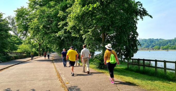 Participants in a wellbeing activity, walking down a tree lined road with a river alongside.