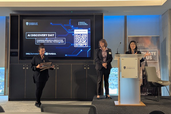 Three people on a stage, one standing behind a lectern.