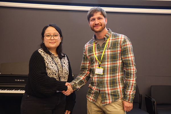 Two people shaking hands and looking into the camera.