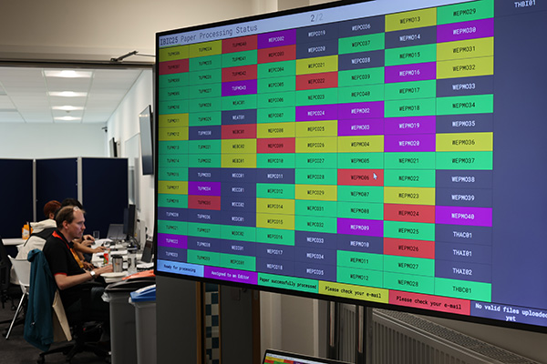 A big computer screen with a colour coded table, people in the background.