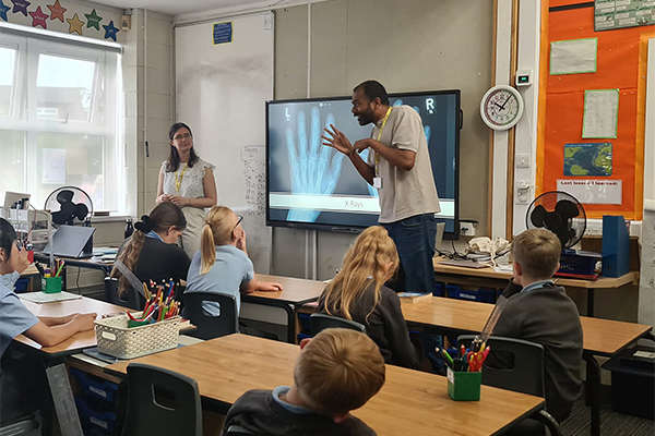 Two students talking to school children in a class room.