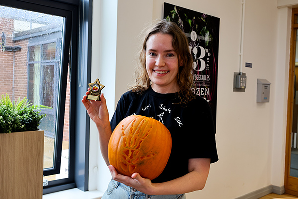 A person holding a trophy and a pumpkin.