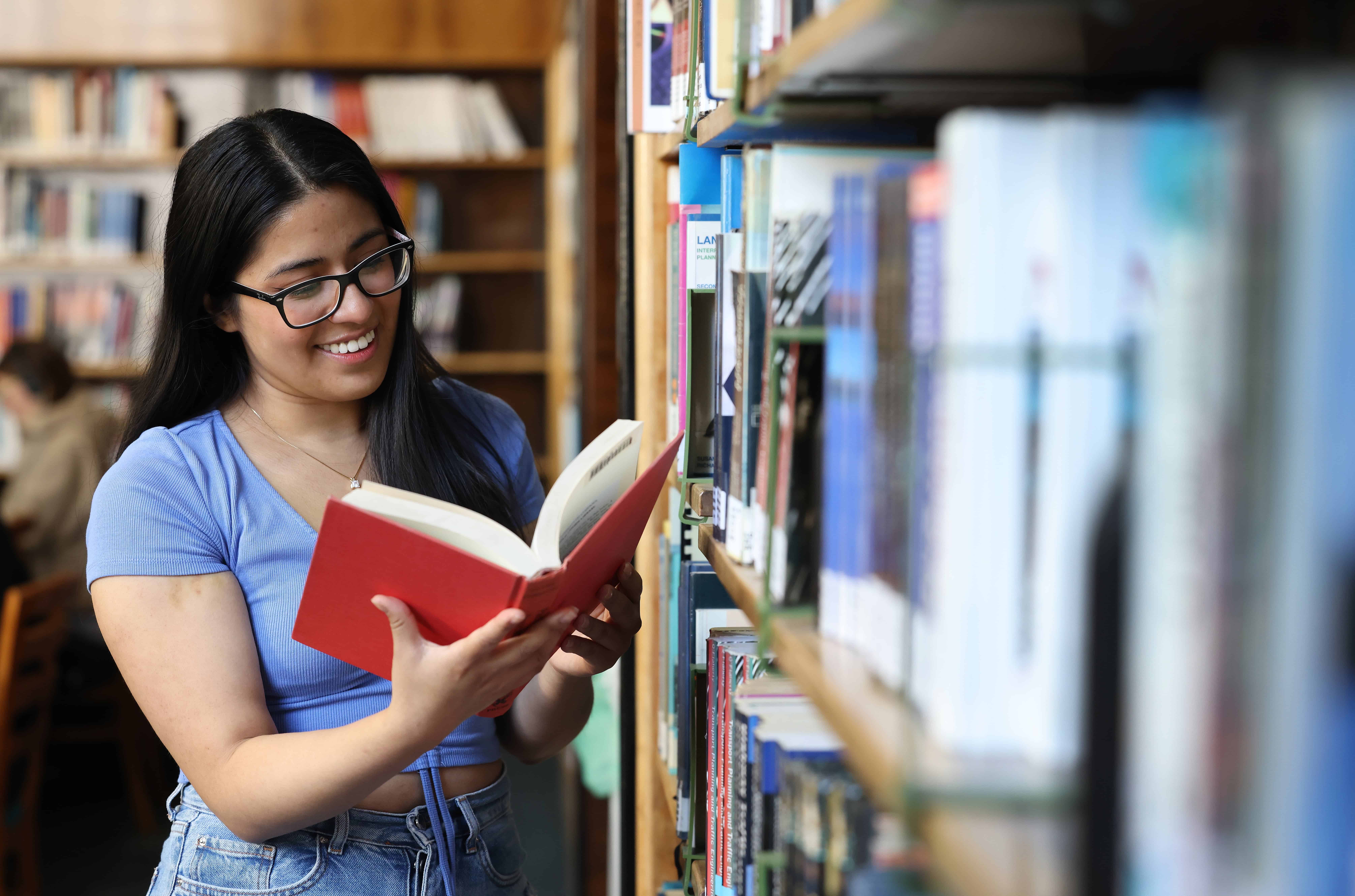 A student reading a red book in the library.