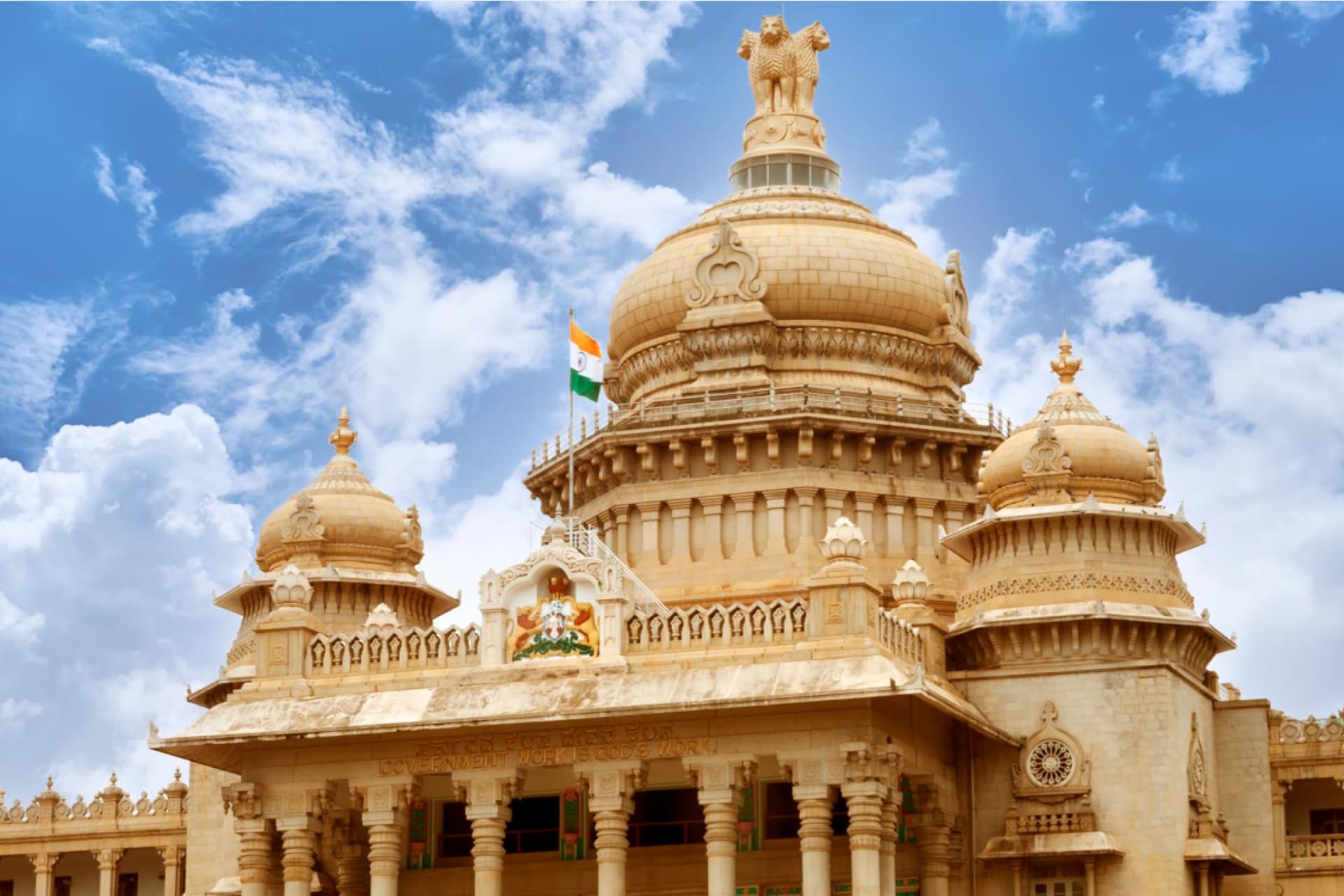 A view of the Vidhana Soudha building in Bengaluru, set against a bright, sunny sky in the background.