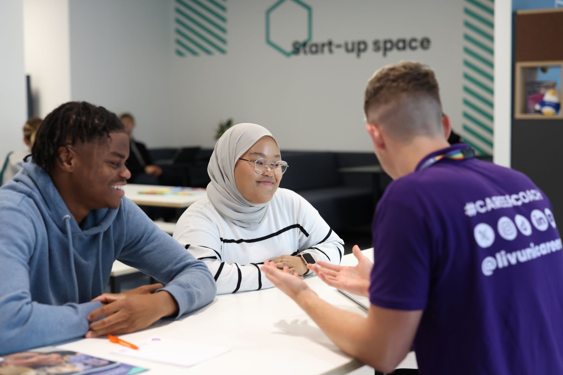 An event taking place at the Sir Peter Rigby Centre shared space, with three people talking at a table.