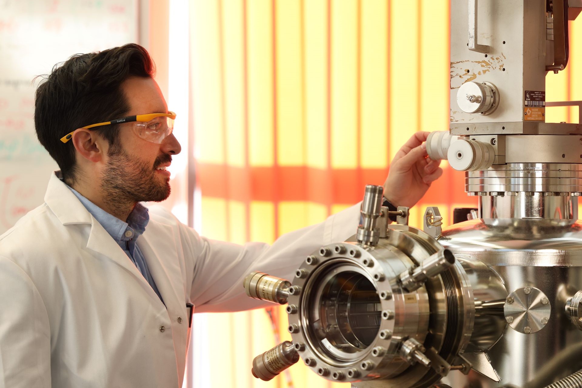A person wearing a lab coat and safety goggles, using a piece of equipment in a lab.