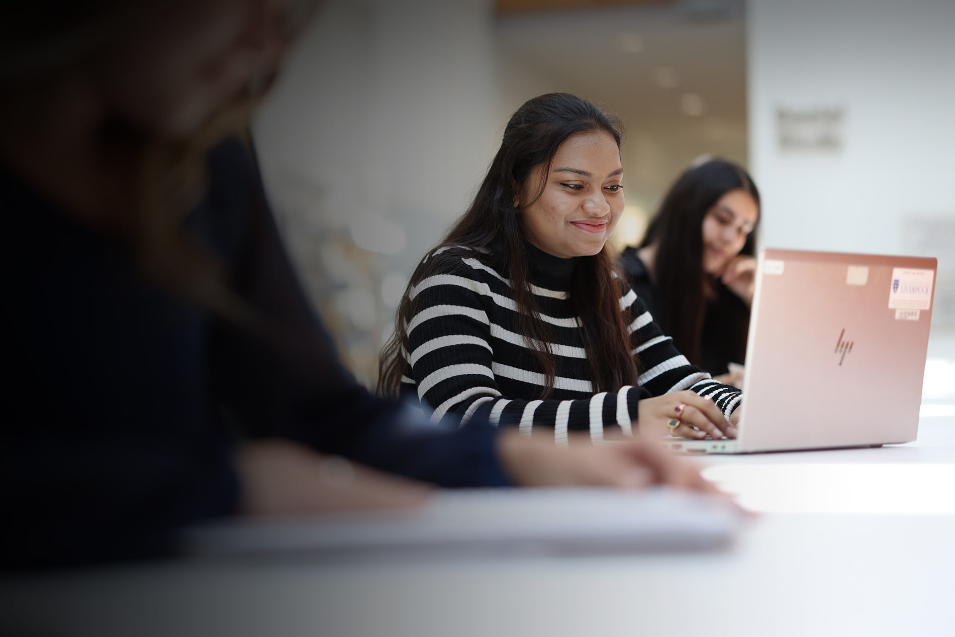A student sitting at a desk, smiling, working on a laptop
