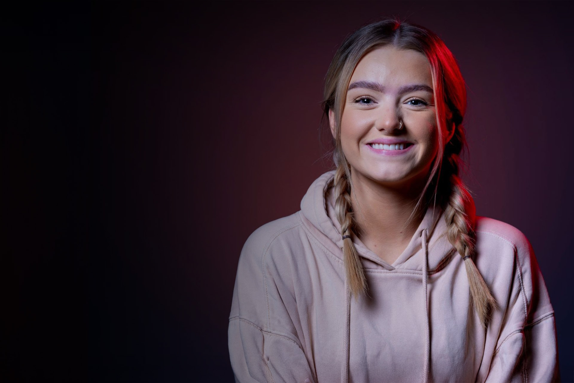 A person looking into the camera and smiling. They are wearing a pink hooded sweatshirt.