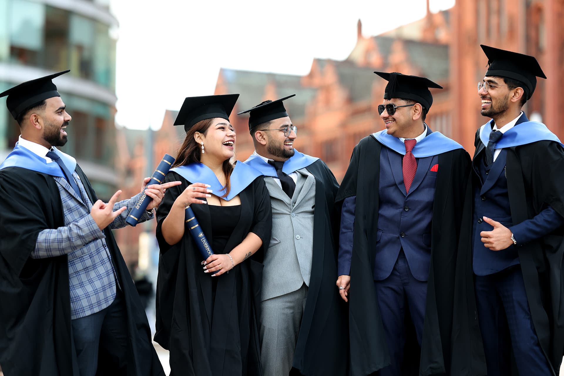 Group of students in graduation gowns and mortarboards outiside the redbrick Victoria building