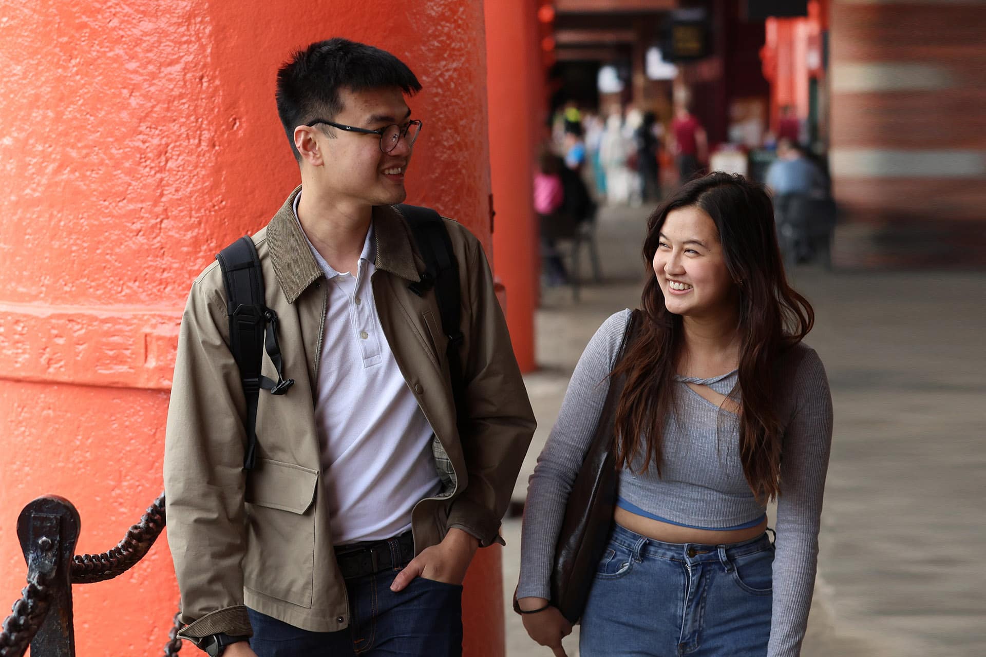 Two people in front of a red pillar at the docks in Liverpool, smiling.