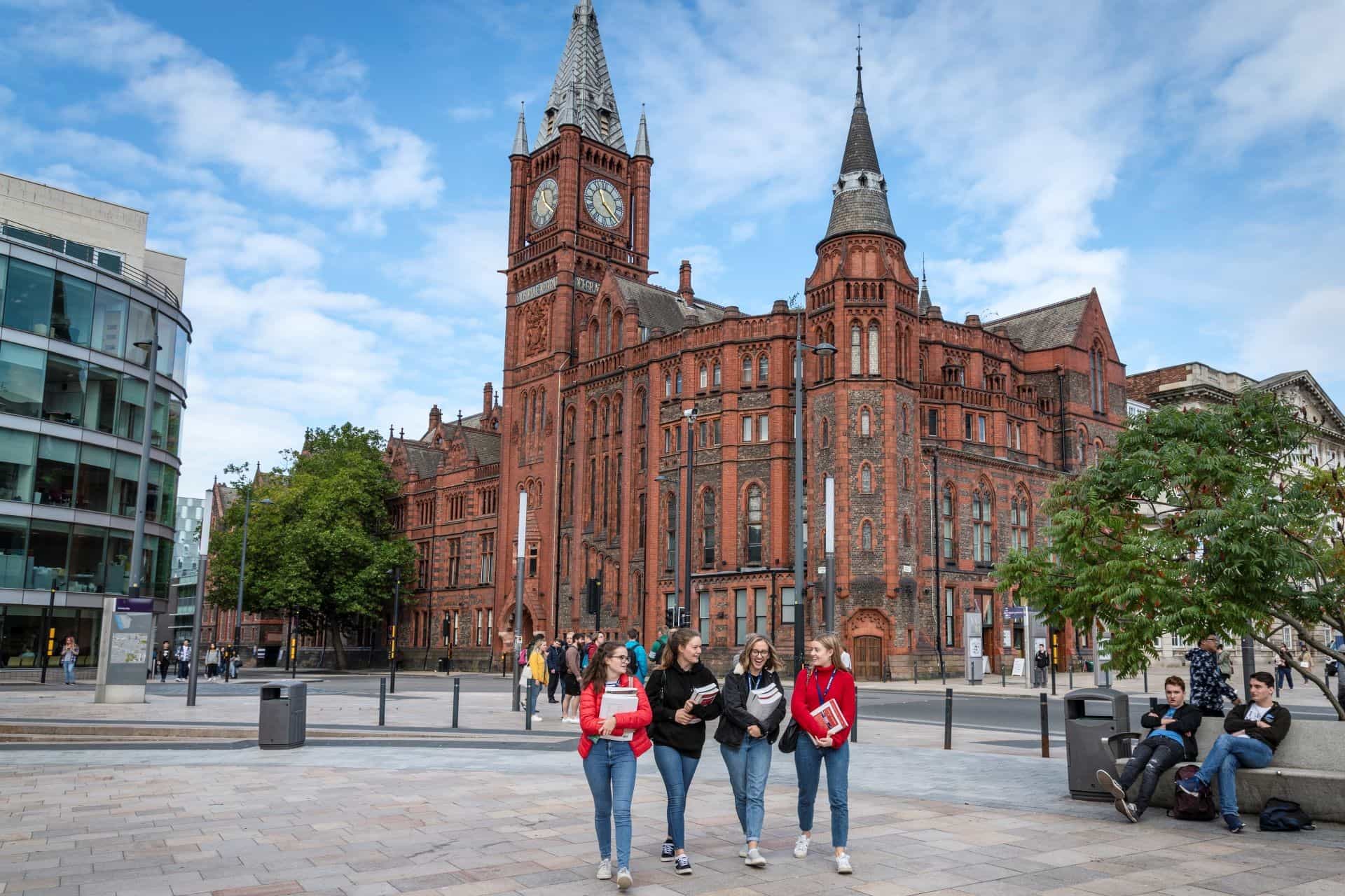 A group of 4 people walking across University Square, with the Victoria Gallery & Museum in the background.